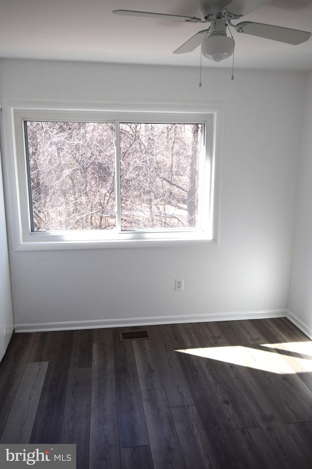 spare room with dark wood-style flooring, a healthy amount of sunlight, visible vents, and baseboards