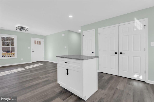 kitchen with dark wood-style flooring, white cabinetry, a kitchen island, and baseboards