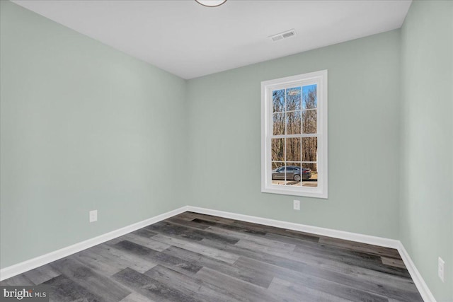 unfurnished room with dark wood-style flooring, visible vents, and baseboards