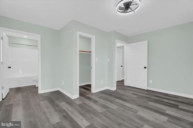 unfurnished bedroom with baseboards, connected bathroom, wood finished floors, a walk in closet, and a closet