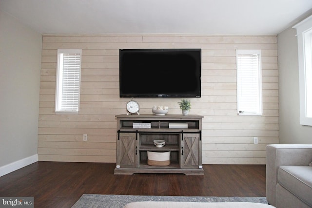 living area with dark wood-type flooring, wood walls, a wealth of natural light, and baseboards