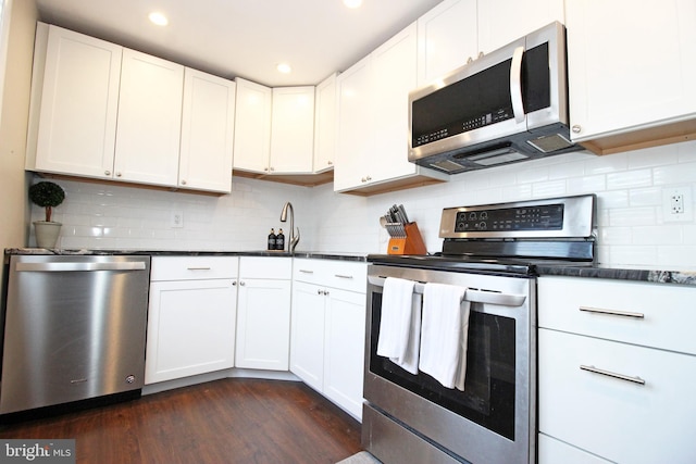 kitchen with stainless steel appliances, dark wood-type flooring, white cabinetry, tasteful backsplash, and dark countertops