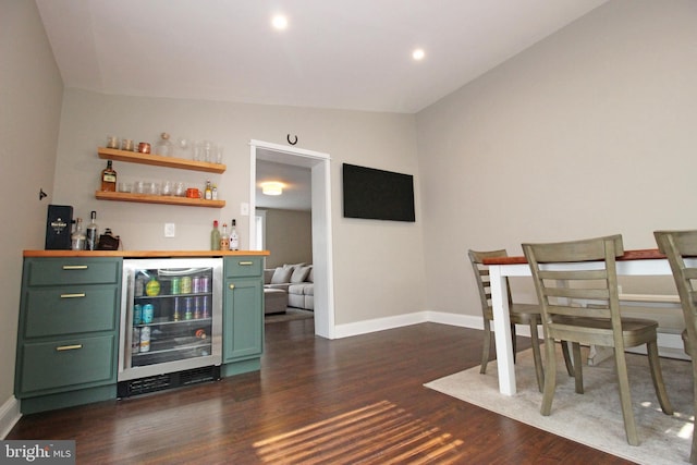 bar featuring wine cooler, dark wood-type flooring, vaulted ceiling, a bar, and baseboards