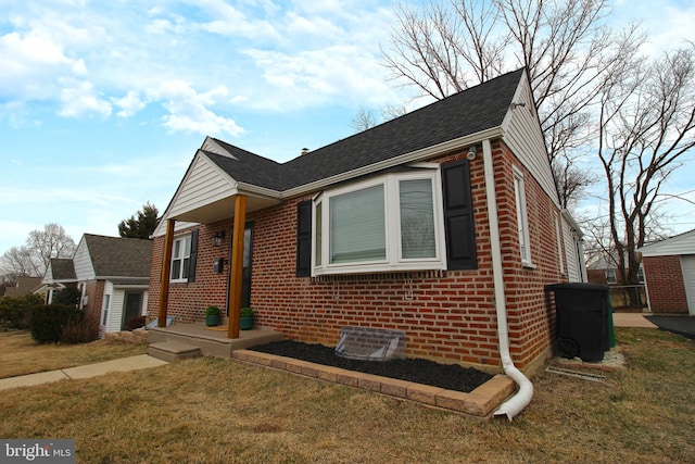 view of front facade featuring a shingled roof, a front yard, and brick siding