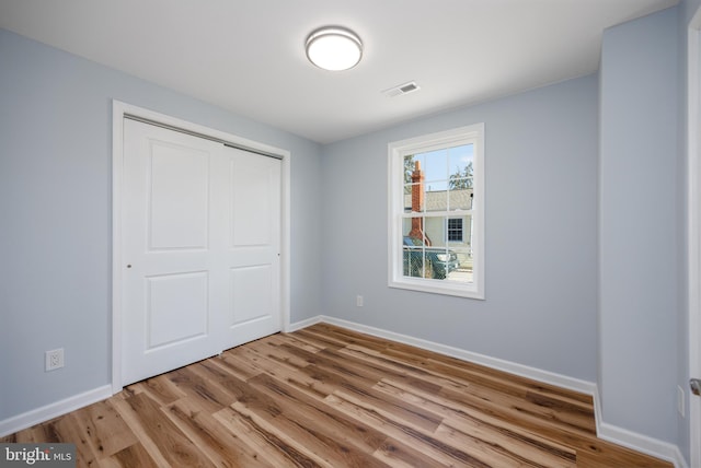 unfurnished bedroom featuring a closet, visible vents, baseboards, and wood finished floors