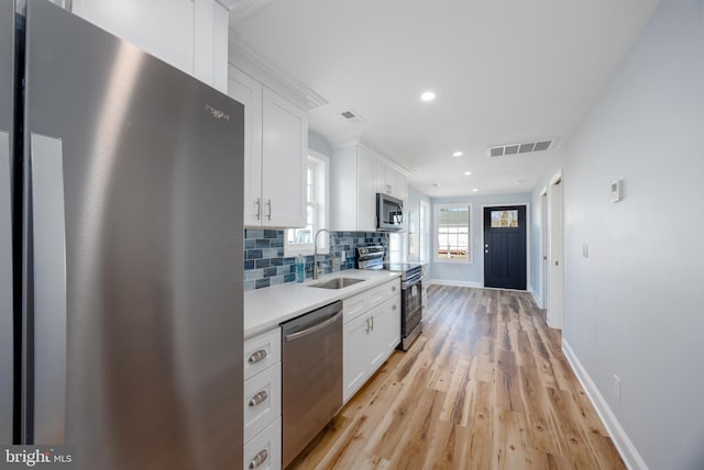 kitchen featuring tasteful backsplash, appliances with stainless steel finishes, light countertops, white cabinetry, and a sink