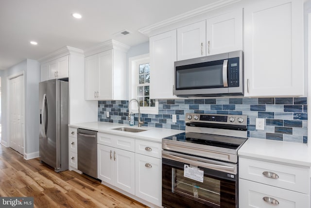 kitchen with light wood-style flooring, appliances with stainless steel finishes, light countertops, white cabinetry, and a sink