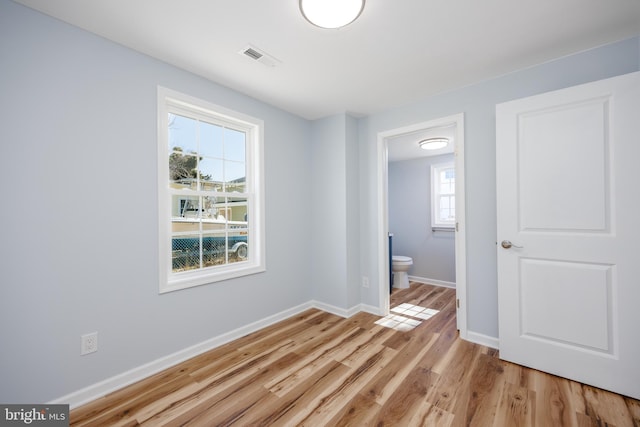 unfurnished bedroom with light wood-style flooring, visible vents, baseboards, and connected bathroom