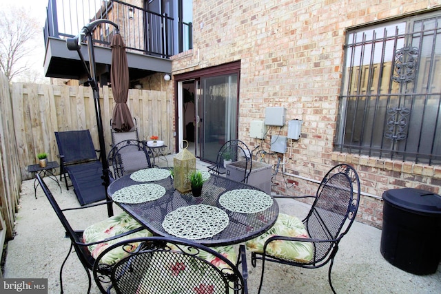 view of patio / terrace with a balcony, outdoor dining area, and fence