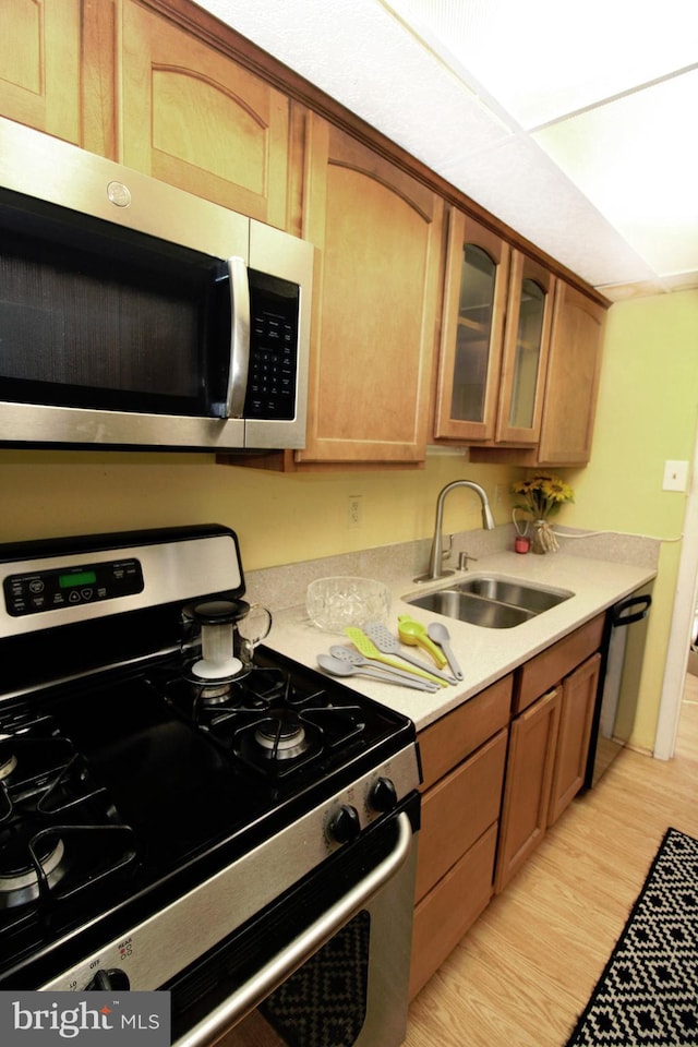 kitchen featuring a sink, stainless steel appliances, light wood finished floors, glass insert cabinets, and light countertops