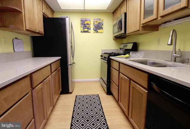 kitchen featuring baseboards, brown cabinets, appliances with stainless steel finishes, light wood-style floors, and a sink