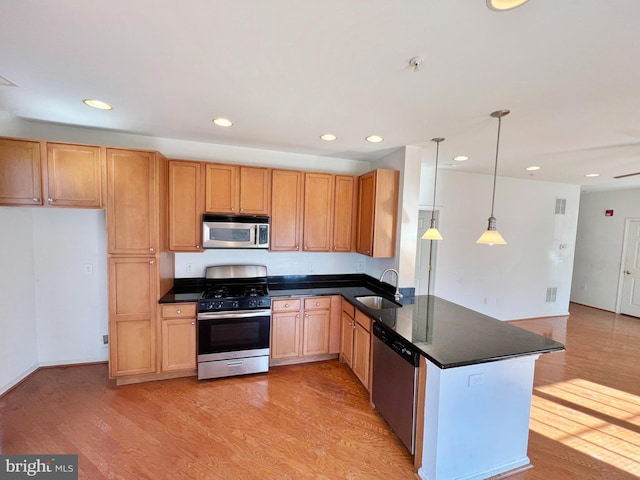 kitchen with light wood-type flooring, dark countertops, appliances with stainless steel finishes, and a sink