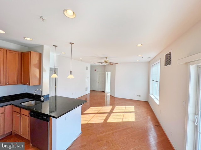 kitchen featuring visible vents, dark countertops, light wood-type flooring, stainless steel dishwasher, and a sink