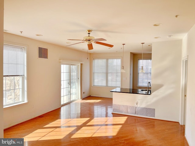 spare room with a healthy amount of sunlight, a sink, visible vents, and wood finished floors