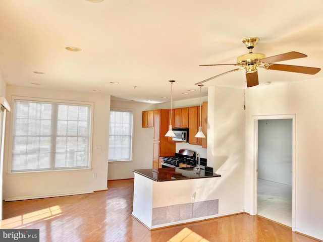 kitchen featuring light wood-style flooring, a sink, appliances with stainless steel finishes, brown cabinetry, and dark countertops