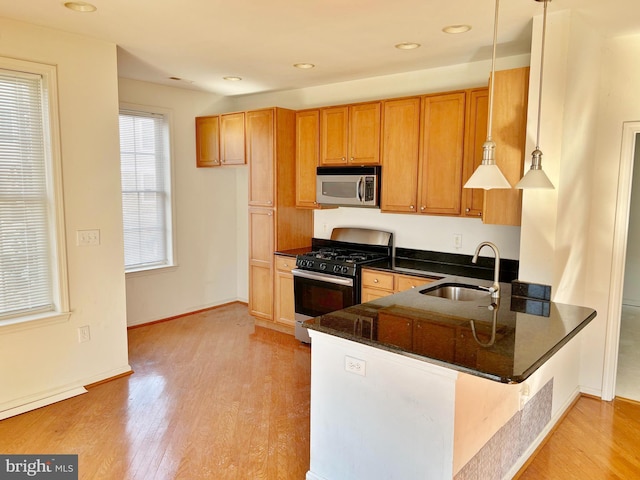 kitchen featuring a peninsula, a sink, light wood-type flooring, stainless steel microwave, and range with gas cooktop