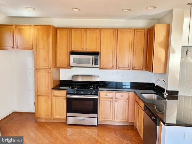 kitchen with recessed lighting, stainless steel appliances, a sink, light wood-type flooring, and dark stone counters