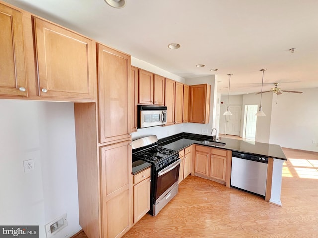 kitchen with dark countertops, appliances with stainless steel finishes, a sink, light wood-type flooring, and a peninsula