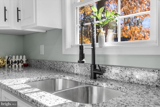 room details with a sink, white cabinetry, and light stone countertops