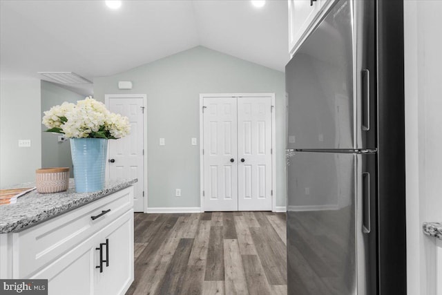 interior space with light stone counters, wood finished floors, white cabinetry, vaulted ceiling, and freestanding refrigerator