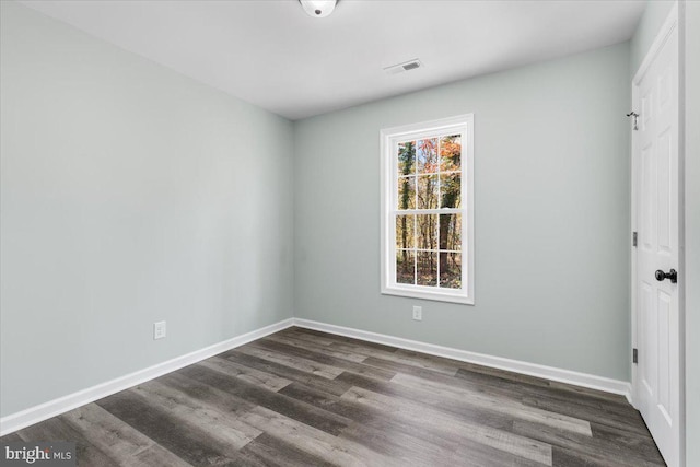 unfurnished room with dark wood-type flooring, visible vents, and baseboards