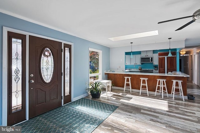 foyer featuring a skylight, crown molding, ceiling fan, wood finished floors, and baseboards