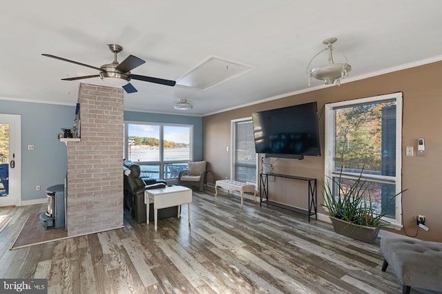 living area with attic access, a wood stove, crown molding, and wood finished floors