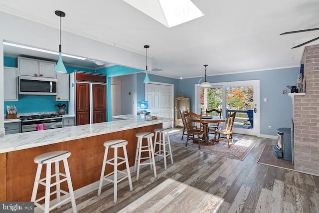 kitchen featuring a skylight, appliances with stainless steel finishes, a breakfast bar, wood finished floors, and ornamental molding