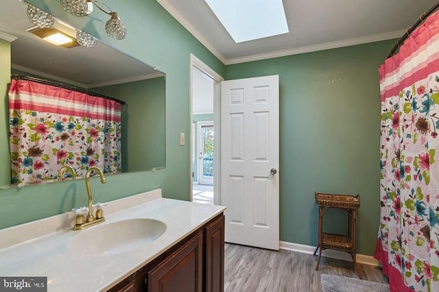 full bathroom with a skylight, wood finished floors, vanity, baseboards, and ornamental molding