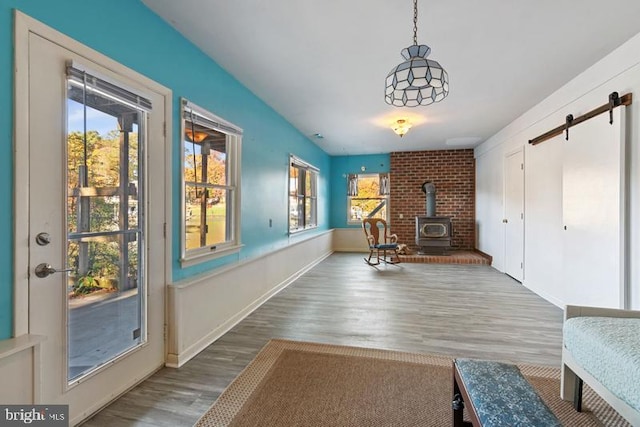 living area featuring a barn door, wood finished floors, a wood stove, and baseboards