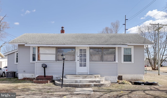 bungalow featuring cooling unit, roof with shingles, and a chimney