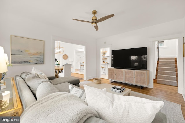 living area with stairway, wood finished floors, and ceiling fan with notable chandelier