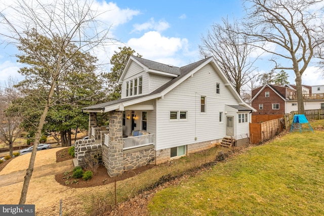 view of side of home featuring roof with shingles, a porch, a lawn, entry steps, and fence