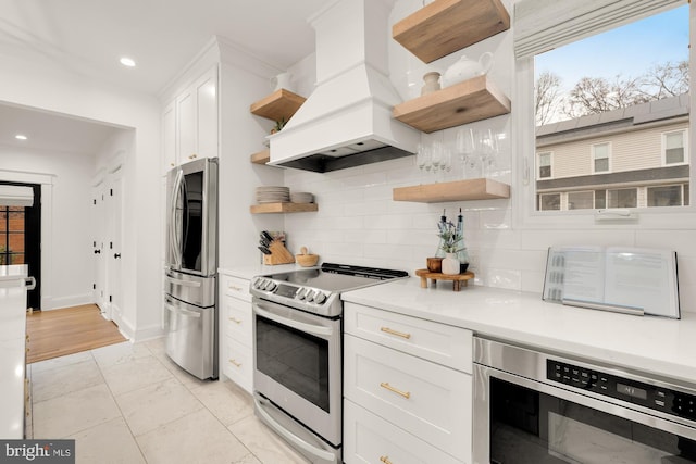 kitchen with premium range hood, white cabinets, light countertops, appliances with stainless steel finishes, and open shelves