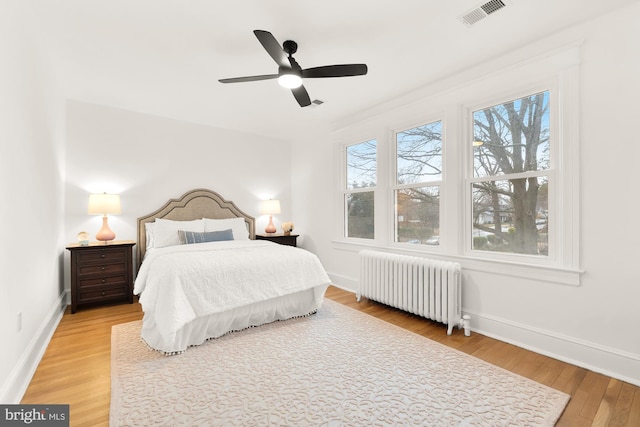 bedroom with a ceiling fan, baseboards, visible vents, light wood-style floors, and radiator heating unit