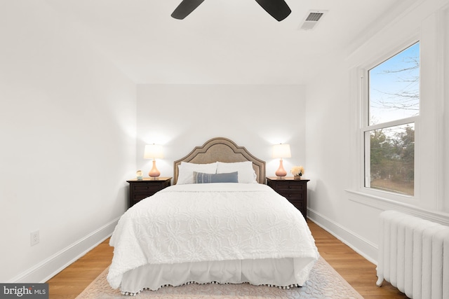 bedroom with light wood-style flooring, radiator heating unit, visible vents, and baseboards