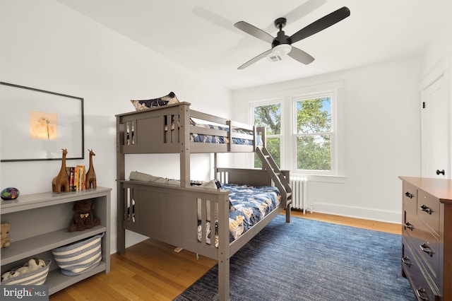 bedroom featuring wood finished floors, visible vents, a ceiling fan, baseboards, and radiator heating unit