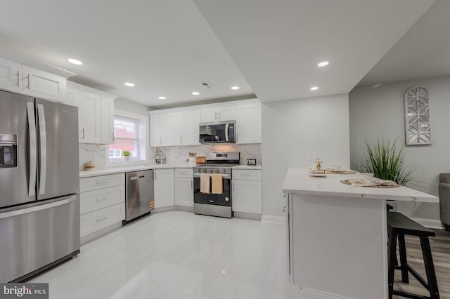 kitchen featuring visible vents, decorative backsplash, appliances with stainless steel finishes, white cabinetry, and a kitchen bar