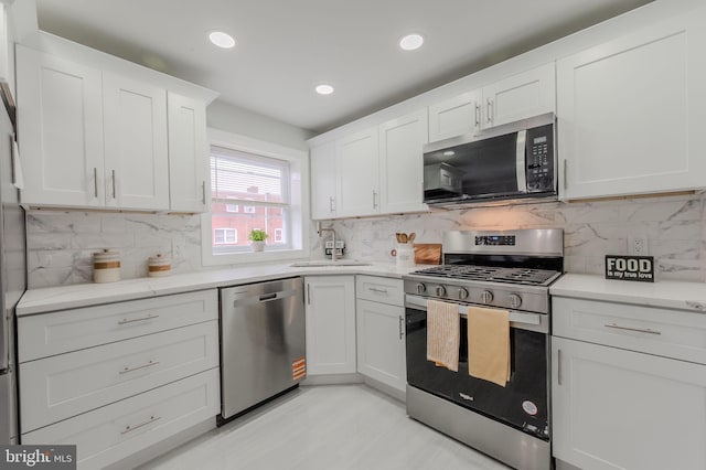 kitchen featuring light stone countertops, stainless steel appliances, white cabinetry, a sink, and recessed lighting