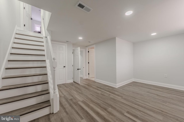 finished below grade area featuring stairway, baseboards, visible vents, and wood finished floors