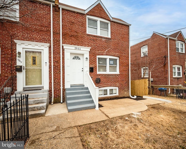 view of property featuring entry steps, brick siding, and fence