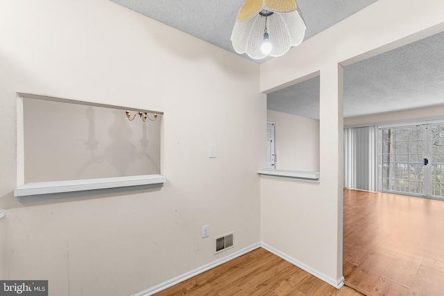 spare room with visible vents, baseboards, a textured ceiling, and wood finished floors