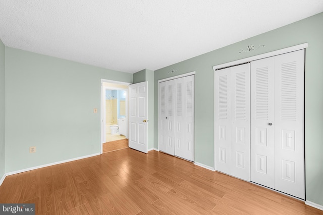 unfurnished bedroom featuring a textured ceiling, baseboards, multiple closets, and wood finished floors