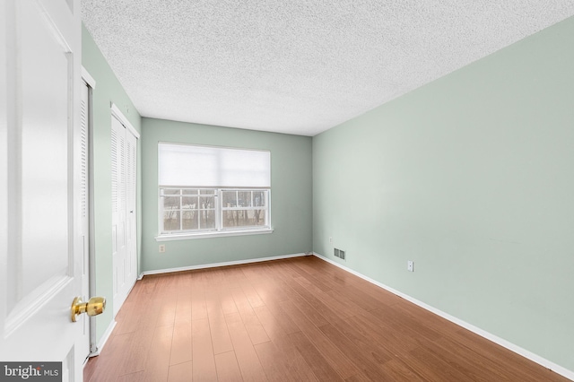 spare room with visible vents, baseboards, a textured ceiling, and wood finished floors