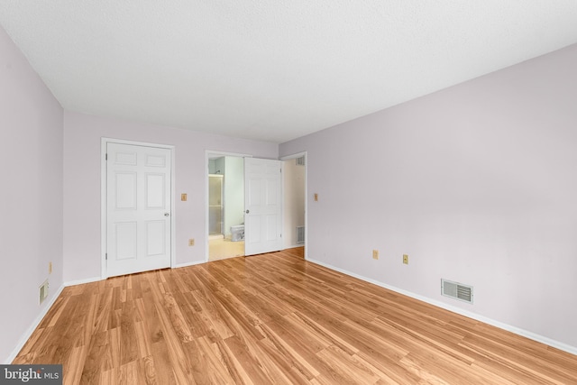 unfurnished bedroom with visible vents, connected bathroom, light wood-type flooring, and baseboards