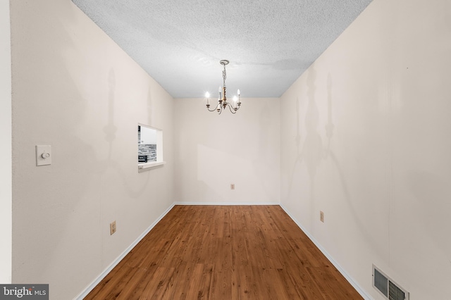 unfurnished dining area with visible vents, baseboards, an inviting chandelier, wood finished floors, and a textured ceiling