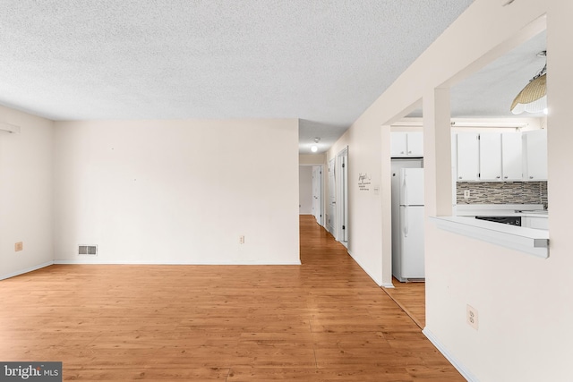 interior space featuring light wood finished floors, visible vents, a textured ceiling, and baseboards