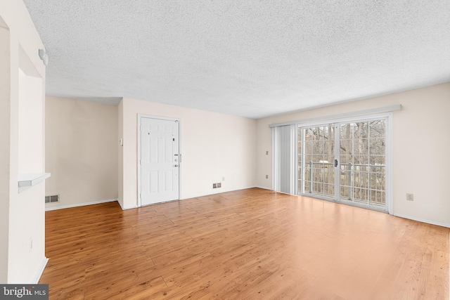 unfurnished living room featuring visible vents, baseboards, a textured ceiling, and wood finished floors