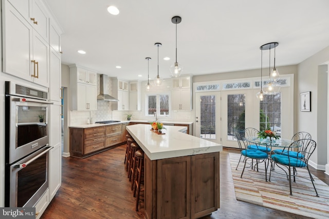 kitchen featuring wall chimney exhaust hood, tasteful backsplash, white cabinets, and stainless steel appliances