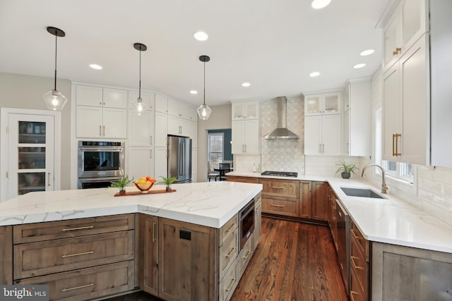 kitchen with white cabinets, wall chimney exhaust hood, a center island, stainless steel appliances, and a sink